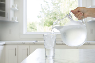 A woman’s hand pouring ice water from a pitcher into a glass.