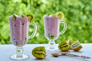 Tasty chia milk pudding in the glass decorated with sliced kiwi fruit and two vintage spoons. Detox superfoods breakfast or healthy dessert on the natural green background. 