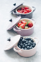 Summer fruit background, top view of berries inside ceramic colored cocotte, blueberries, strawberries, raspberries, flat lay, blue table. Detox and healthy food concept.