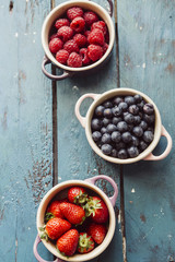 Summer fruit background, top view of berries inside ceramic colored cocotte, blueberries, strawberries, raspberries, flat lay, blue table. Detox and healthy food concept.