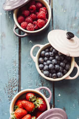 Summer fruit background, top view of berries inside ceramic colored cocotte, blueberries, strawberries, raspberries, flat lay, blue table. Detox and healthy food concept.