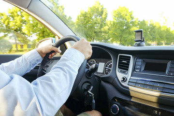 Close up of young man hands holding steering wheel while driving car. Dashboard panel, phone holder mount, windshield. Male business man inside vehicle interior in a daylight. Background, side view.