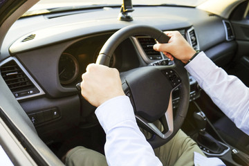 Close up of young man hands holding steering wheel while driving car. Dashboard panel, phone holder mount, windshield. Male business man inside vehicle interior in a daylight. Background, side view.