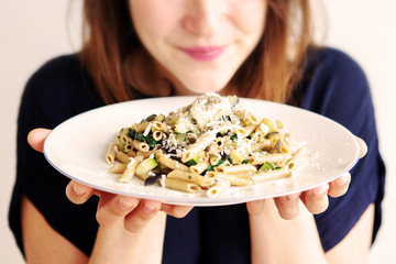 young woman holding a white plate with pasta and cheese
