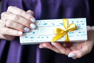 Present box with a gold bow with macaroons inside. Woman holds a box with biscuits.