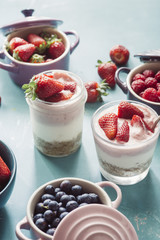Strawberry cheesecake inside glass jar over a blue background and  top view of berries , inside ceramic colored cocotte, blueberries, strawberries, raspberries, flat lay