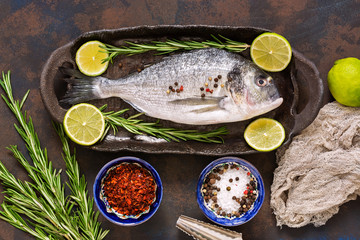 Fresh fish with spices on a dark background, top view. Raw dorado fish on a ceramic dish with lime and rosemary.