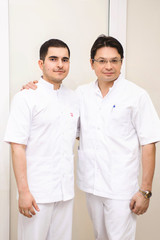 Cheerful group of young dentists and their assistants standing in the dental office and looking at camera and friendly smiling at white background of medical room.