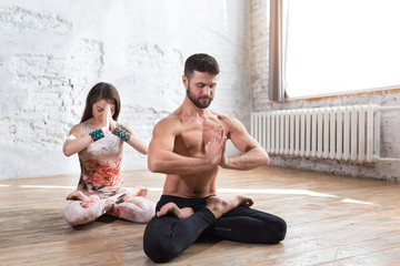 Fototapeta na wymiar Fitness young yoga couple meditating at loft studio with white brick wall and windows with sunlight. Woman and man relaxing in lotus position, calm and zen moment concept