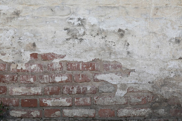 old wall from a red brick plastered from above and covered with white paint. Plaster in places has disappeared and has bared an old bricklaying with a regular laying. horizontal direction
