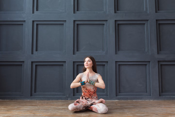 Attractive woman practicing yoga, while sitting in Lotus pose, working out on grey wall background...