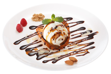 Ice cream ball decorated with chocolate syrup, nuts, raspberries, mint leaves and coconut chips on a wafer of coconut and honey. All on white plate isolated on white background.