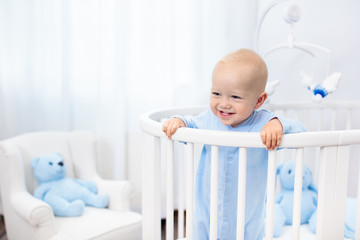 Baby boy standing in bed in white nursery