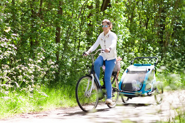 Mother on bicycle with baby bike trailer in park