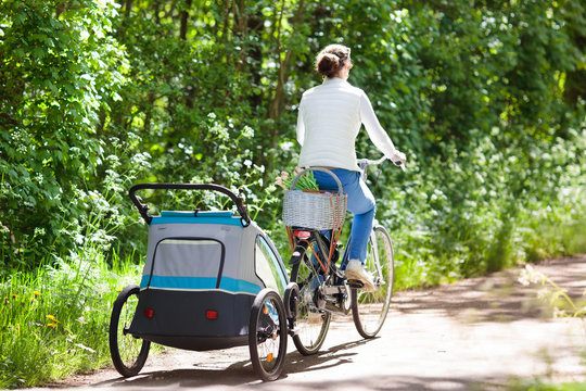 Mother on bicycle with baby bike trailer in park