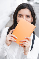 Female student holding a colorful notebook and smiling behind it