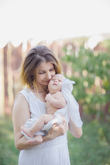 A beautiful young mother with a baby in her arms is standing in the garden.