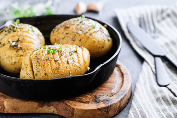 Close-up of homemade baked potato with olive oil, garlic, rosemary, mustard, dill and black pepper in a cost fry pan.