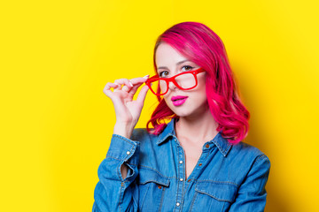 Young pink hair girl in blue shirt and red glasses. Portrait isolated on yellow background