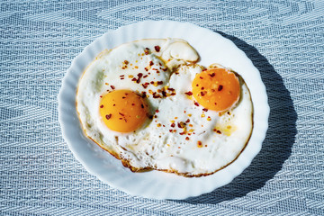 Fried eggs on a plate with chili peper.