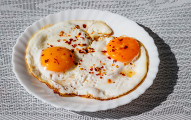 Fried eggs on a plate with chili peper.