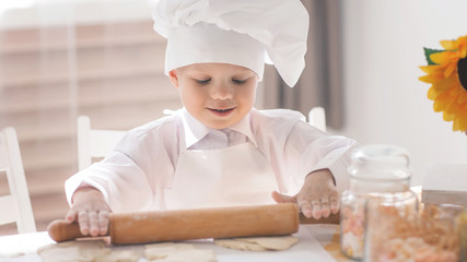 A small child in the form of a cook rolls the dough on a table