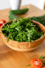 Wooden Bowl of fresh green, natural arugula with red tomatoes on a wooden background