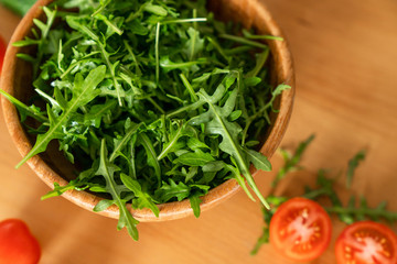 Wooden Bowl of fresh green, natural arugula with cherry tomatoes on a wooden background