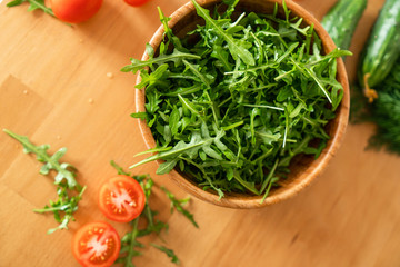 Wooden bowl of fresh green, natural arugula with cherry tomatoes and cucumbers on a wooden background