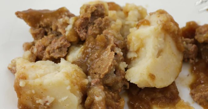 Close video of a meatloaf with mashed potatoes and gravy TV dinner on a white plate being stirred with a fork then taking a forkful at the end.