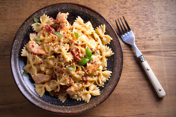 Pasta with chicken, sun dried tomatoes and basil in creamy mozzarella sauce in bowl on wooden table. overhead, horizontal