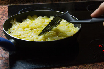 Traditional Spanish potato omelette cooking in frying pan on glass ceramic hob