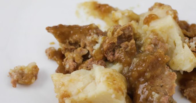 Close video of a meatloaf with mashed potatoes and gravy TV dinner being dumped onto a white plate.