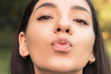 Portrait of a beautiful young girl, kissing, face close-up, nature as background