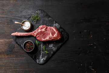 Raw Tomahawk steak on wooden background with spices for grilling, top view, copy space