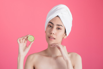 beautiful asia woman with towel on head with perfect clean skin smiling holding cucumber slices over pink background. Beauty cosmetology and spa.