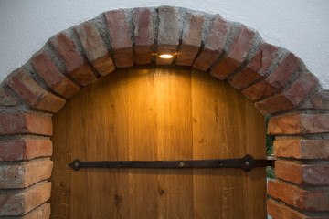 Antique wooden door with a arch frame of bricks lighted by a single lamp