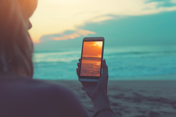 Girl looking at the photo on smartphone while enjoying the ocean / sea sunset.