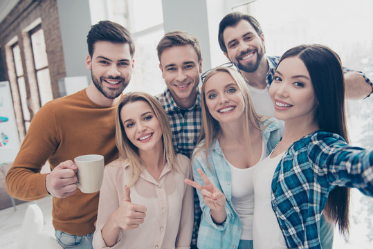 Self portrait of cheerful, joyful, positive students managers shooting selfie on front camera in modern office showing two fingers, like, peace, hi sign, holding cup with coffee, partnership