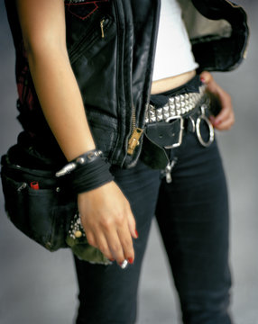 Young adult wearing studded belt and holding cigarette.