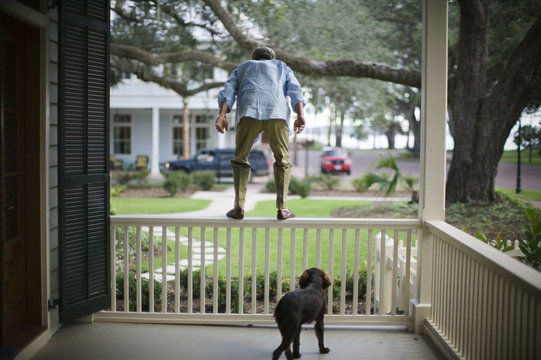 Mature man being watched by his dog while preparing to jump from a balcony railing.