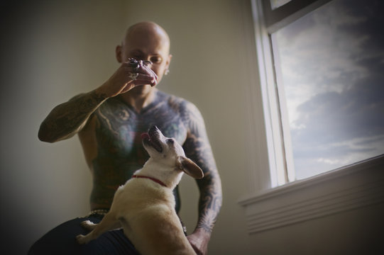 A tattooed man is playing with his pet dog.