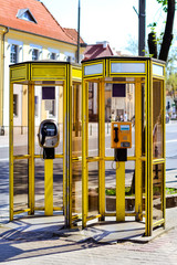 Yellow glass telephone booths with payphones are located on a pedestrian street. Obsolete means of telephone communication in free access. Bialystok, Poland