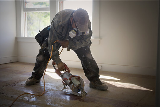 Male builder sanding floorboards with a power tool inside a room.