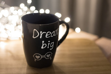 Grey mug with text Dream big on a wooden cutting board and lights bokeh on background. Copyspace