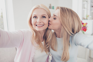 Self portrait of cheerful lovely cute charming daughter kissing in cheek mother family with one...