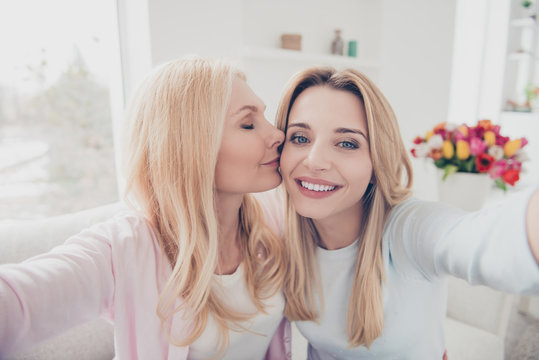 Self portrait of cheerful lovely cute charming mother kissing in cheek daughter family with one parent shooting selfie on front camera enjoying time meeting holiday day indoor