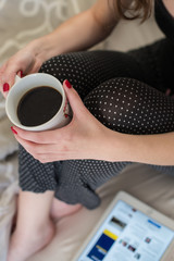 Woman with Red Nails in pajamas holding coffee mug in bed