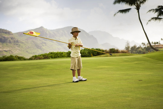A boy holding a golf flag on the golf course