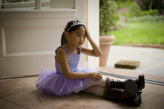 Sitting young girl wearing a tutu and tiara.